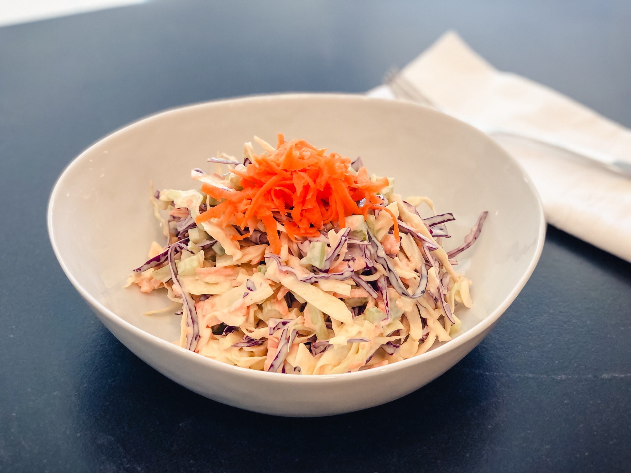 A bowl of deliciously colorful coleslaw with a dollop of grated carrot on top. 